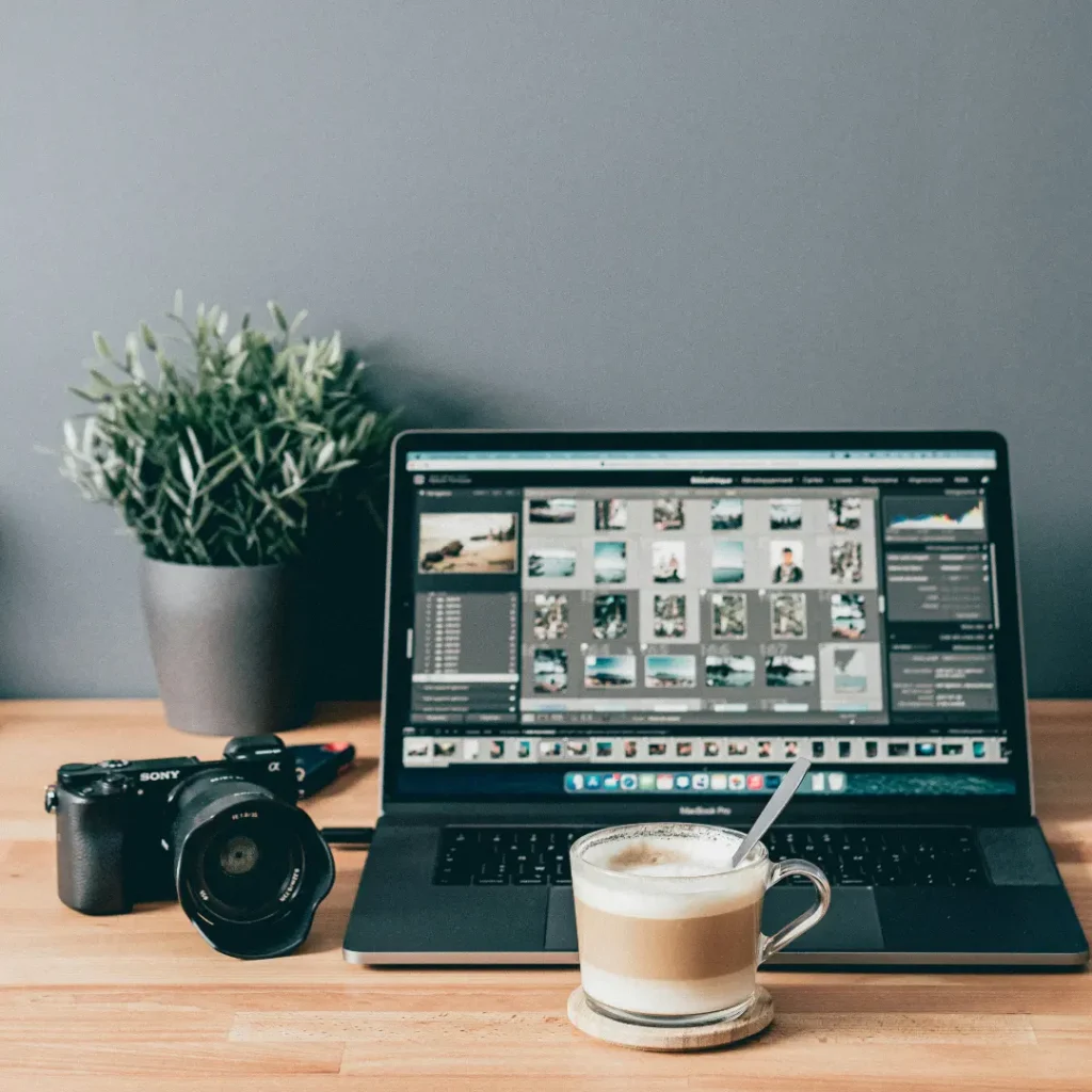 Laptop, a cup of coffee, and camera on top of a table in "How to Choose a Photo Editing Service" article in Dropicts.com