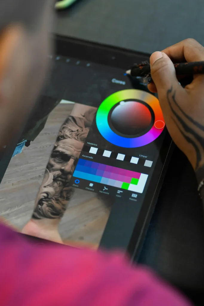 A person using a stylus pen to adjust photo editing sliders (like contrast and light) on a digital tablet next to a camera lens resting on the desk. This image is located in "Photo Editing Quote" article in Dropicts.com website.