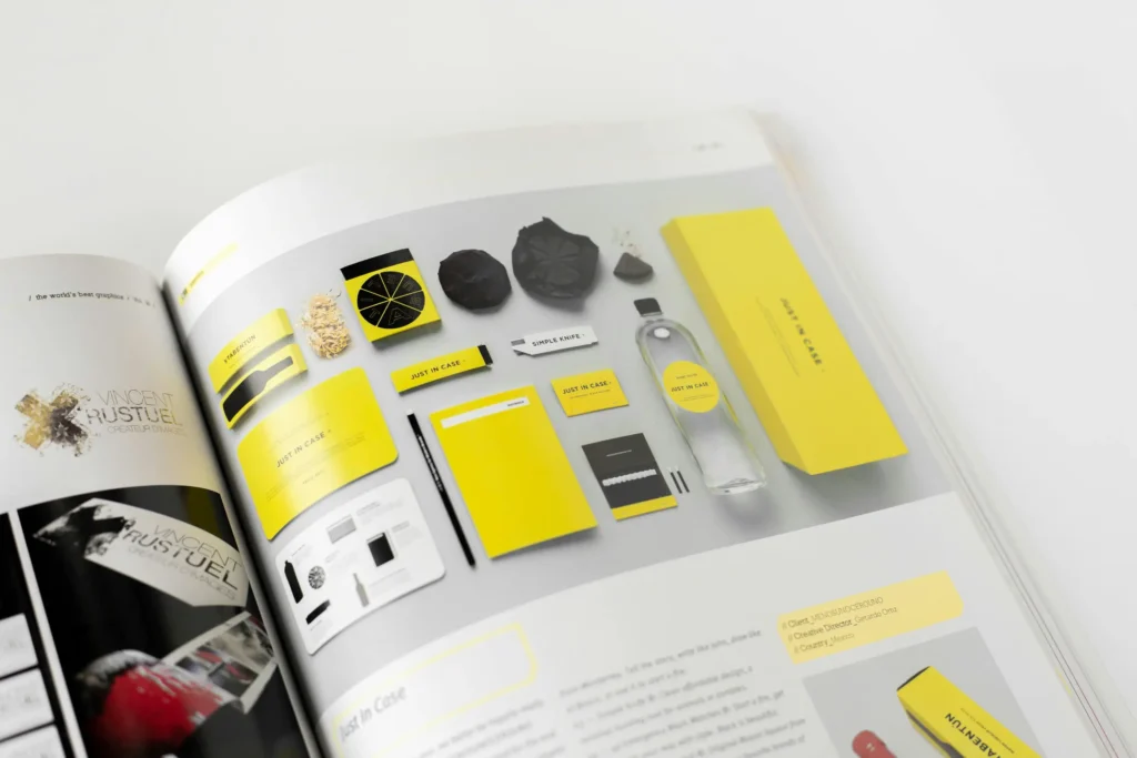 An open design book displaying a flat lay photograph of a yellow and black branding kit that includes boxes, a water bottle, and a pencil, with the text "JUST IN CASE" printed on several items. This image is included in "Product Photography for Wholesale Line Sheets" in Dropicts.com website